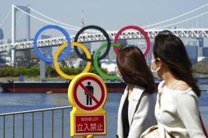 Women walk by a "no trespassing" sign at a park with a backdrop of the Olympic rings floating in the water in the Odaiba section Thursday, March 18, 2021, in Tokyo. Tokyo Olympics creative director Hiroshi Sasaki is resigning after making demeaning comments about Naomi Watanabe, a well-known female celebrity. Sasaki who was in charge of the opening and closing ceremonies for the Olympics, told planning staff members last year that Watanabe could perform in the ceremony as an “Olympig.” (AP Photo/Eugene Hoshiko)