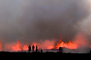 People watch flowing lava during an volcanic eruption near Litli Hrutur, south-west of Reykjavik in Iceland on July 10, 2023. A volcanic eruption started on July 10, 2023 around 30 kilometres (19 miles) from Iceland's capital Reykjavik, the country's meteorological office said, marking the third time in two years that lava has gushed out in the area. "The eruption is taking place in a small depression just north of Litli Hrutur, from which smoke is escaping in a north-westerly direction," the office said. Footage circulating in the local media shows a massive cloud of smoke rising from the ground as well as a substantial flow of lava. (Photo by Kristinn Magnusson / AFP) / Iceland OUT