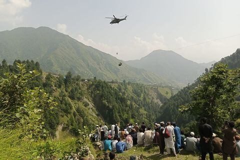 La gente observa cómo un soldado del ejército desciende de un helicóptero durante una misión de rescate para recuperar a los estudiantes atrapados en un telesilla en la aldea pastún de la provincia montañosa de Khyber Pakhtunkhwa, el 22 de agosto de 2023.