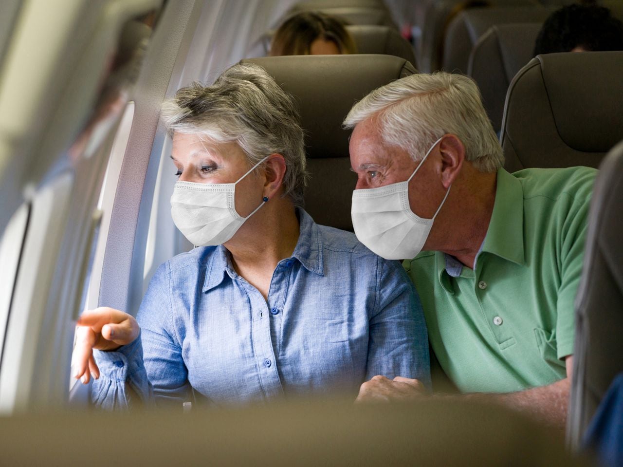 Pareja de ancianos latinoamericanos viajando en avión con mascarillas y mirando por la ventana - viaje durante la pandemia de COVID-19