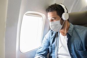 Retrato de un latinoamericano que escucha música mientras vuela en un avión con mascarilla para evitar el coronavirus.