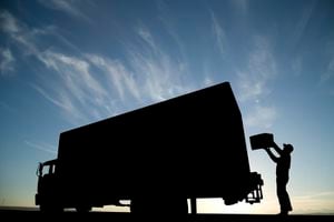 A silhouette of a courier putting a package a delivery truck.