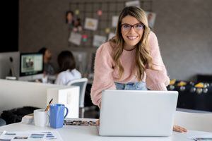 Retrato de una mujer joven feliz trabajando en línea en una oficina creativa usando su computadora portátil y sonriendo