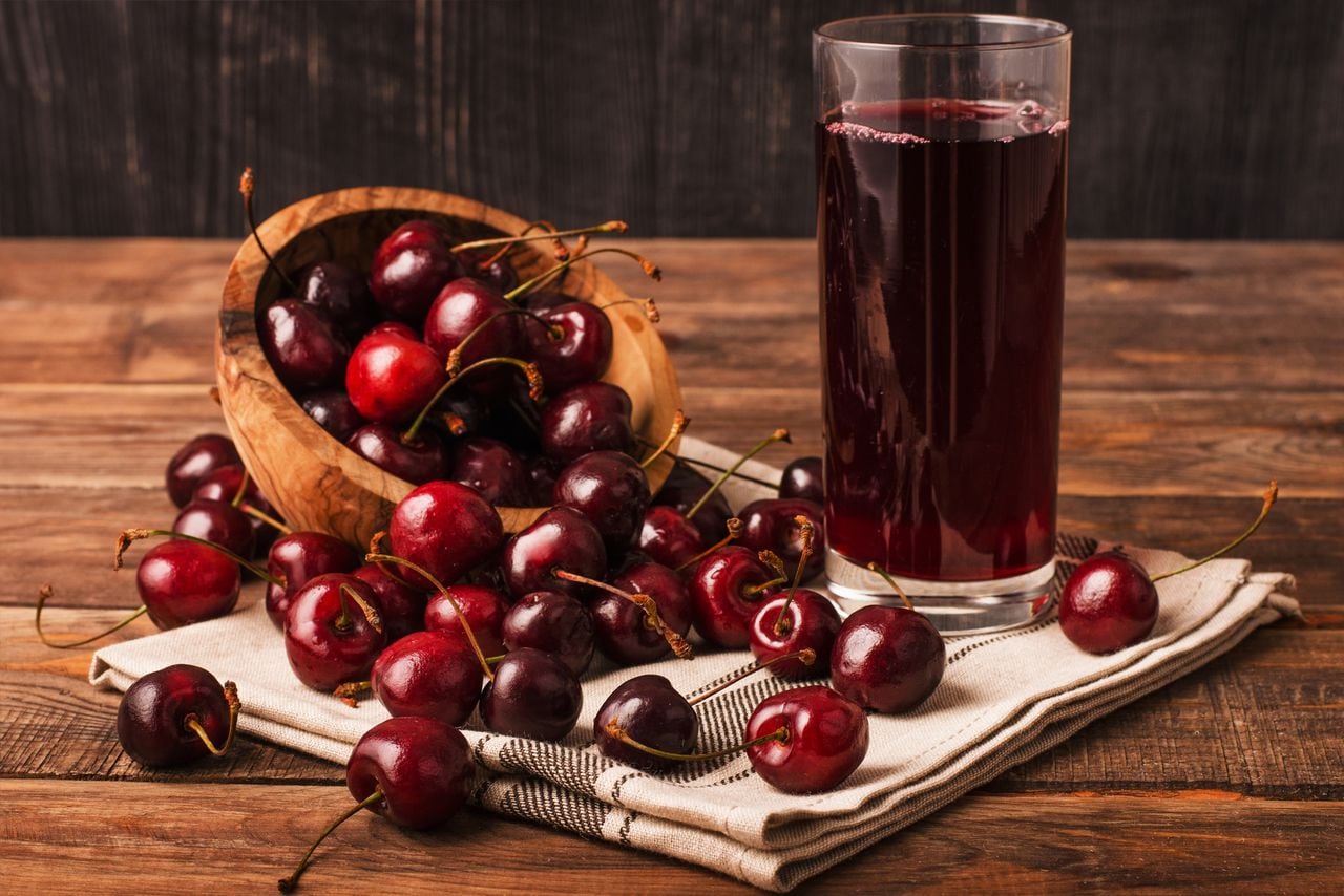 Cold cherry juice in a glass with ripe berries in bowl basket on a wooden table