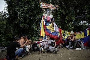 Los migrantes se sientan bajo un cartel que marca la frontera entre Panamá y Colombia durante su viaje por el Tapón del Darién, el martes 9 de mayo de 2023. Las restricciones de asilo de EE. UU. relacionadas con la pandemia, conocidas como Título 42, expirarán el jueves 11 de mayo. (AP Photo/Ivan Valencia)