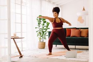Longitud total de mujer sana haciendo ejercicio en casa viendo videos en línea en la computadora portátil. Hermosa mujer en ropa deportiva haciendo yoga.