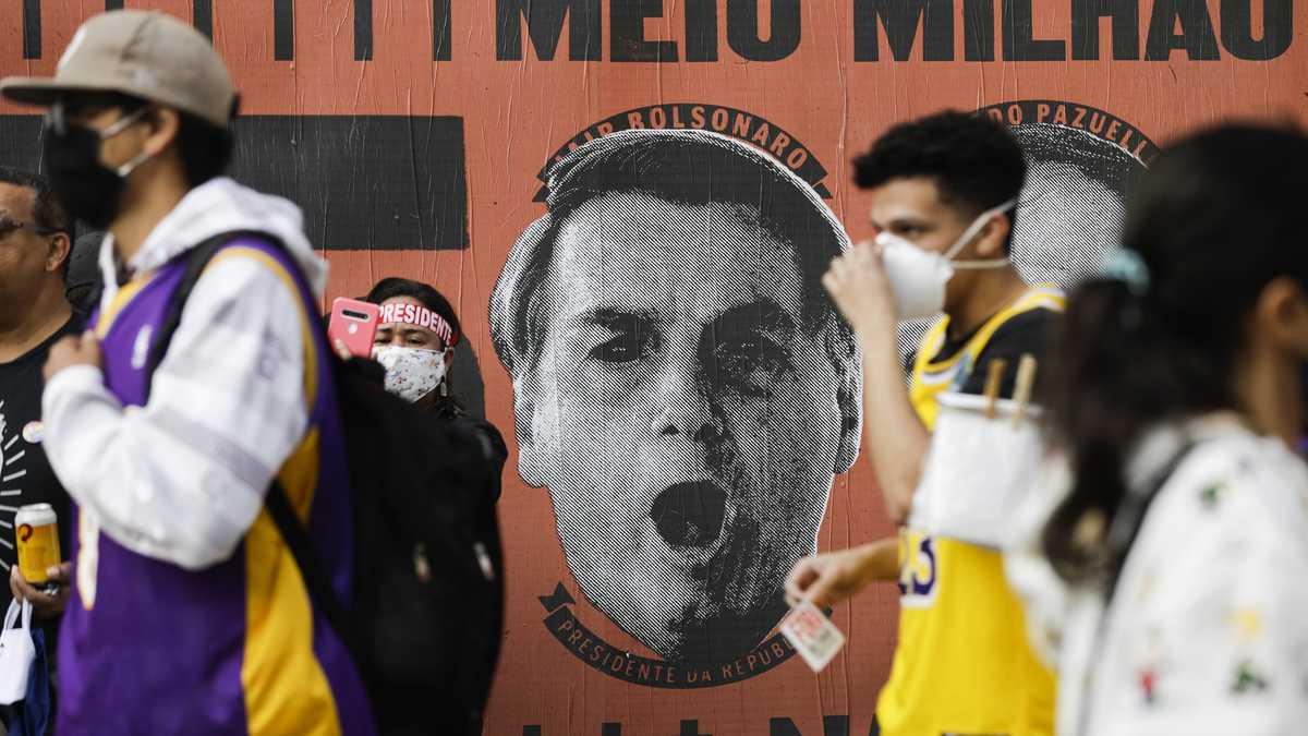 Manifestantes caminan frente a un mural que representa el rostro del presidente brasileño Jair Bolsonaro durante una manifestación contra el manejo de Bolsonaro de la pandemia de coronavirus y las políticas económicas.  (AP Photo/Marcelo Chello)
