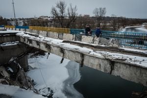 Elena (derecha) y Petr cruzan un puente destruido después de recolectar agua potable de un punto de distribución en Kupiansk el 13 de febrero de 2023, en medio de la invasión rusa de Ucrania. (Foto de YASUYOSHI CHIBA / AFP)