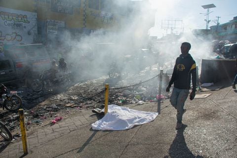 Contenido gráfico / Un hombre pasa junto al cuerpo de una persona que estaba entre una docena asesinada en la calle por pandilleros, en Ptionville, Puerto Príncipe, Haití, el 18 de marzo de 2024.