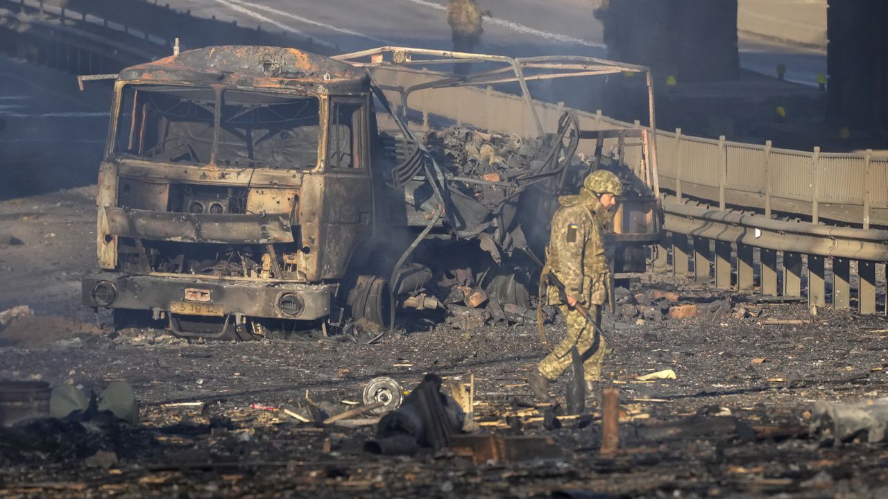 Un soldado ucraniano se desplaza entre los restos de un camión militar incendiado en una calle en Kiev, Ucrania, el sábado 26 de febrero de 2022. (AP Foto/Efrem Lukatsky)
