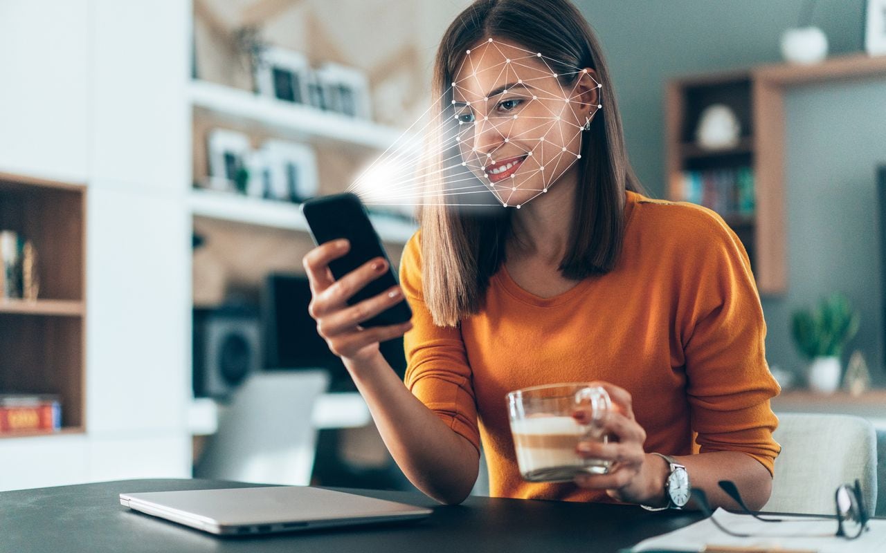 El software de reconocimiento facial escanea el rostro de una mujer joven que sostiene un teléfono inteligente en casa