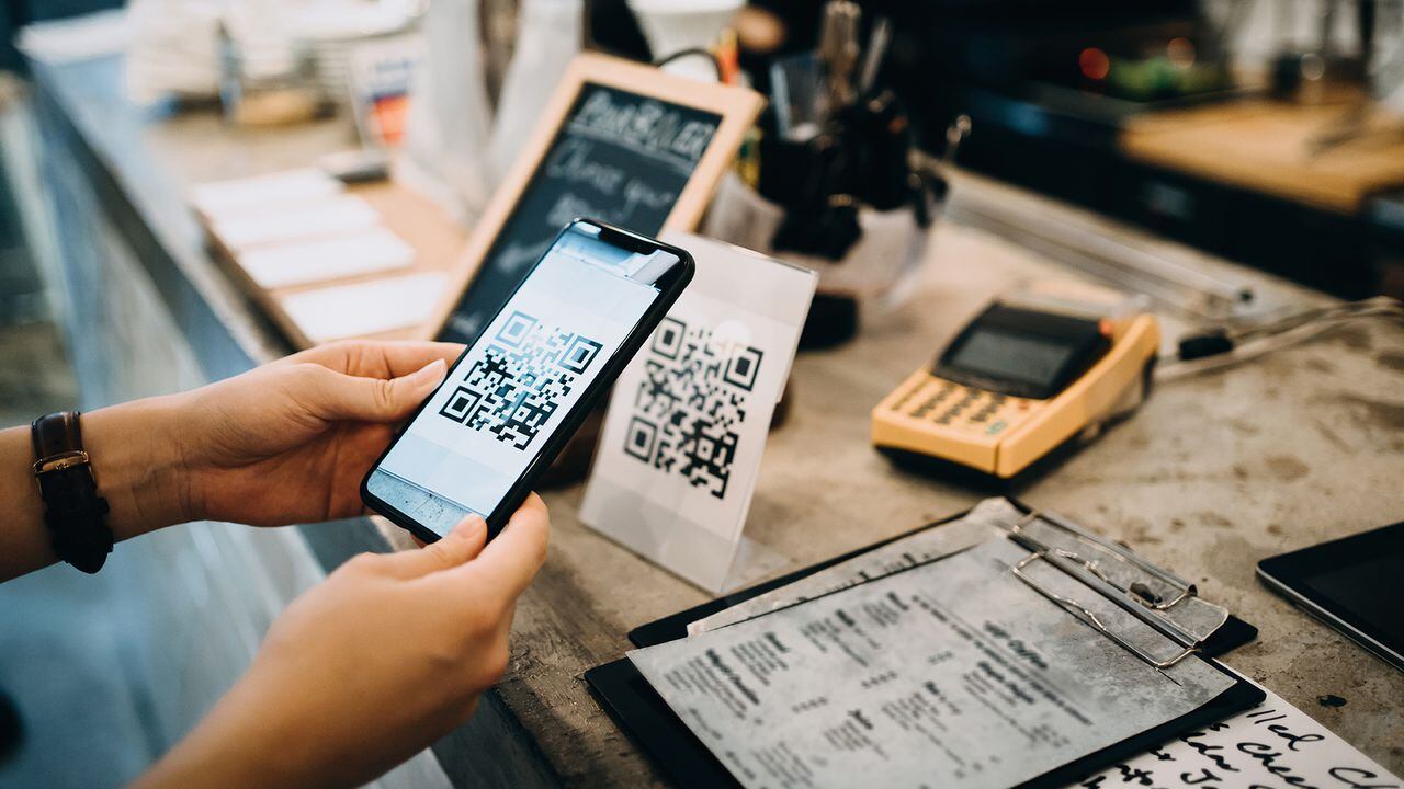 Customer scanning QR code, making a quick and easy contactless payment with her smartphone in a cafe