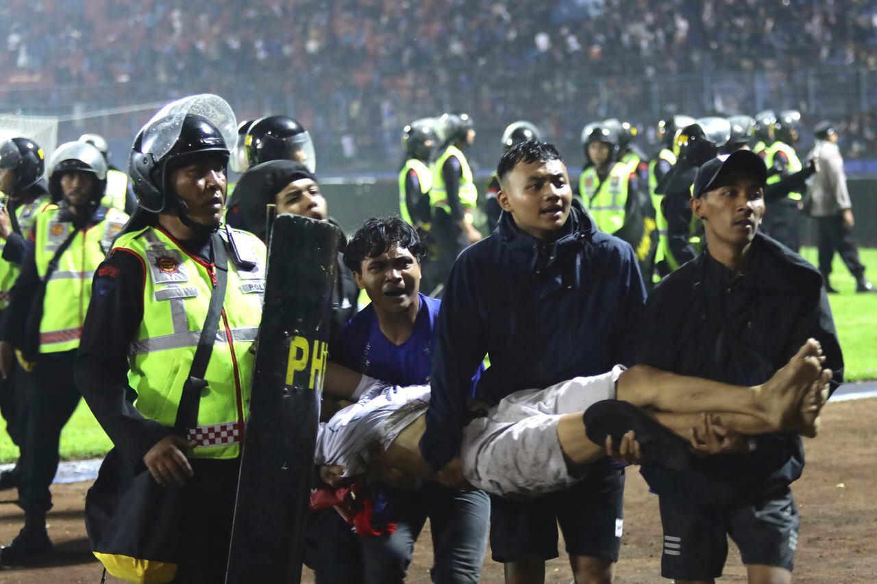 Un grupo de aficionados carga a un hombre herido en los enfrentamientos durante un partido de fútbol en Malang, Indonesia, el sábado 1 de octubre de 2022