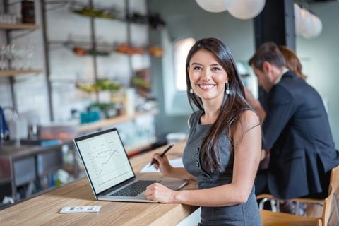 Mujer de negocios feliz trabajando en un café en una computadora portátil y mirando a la cámara sonriendo. La imagen en pantalla es de diseño propio.