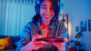 Happy asia girl gamer use la competencia de auriculares, juegue videojuegos en línea con luces de neón coloridas para teléfonos inteligentes en la sala de estar en casa.