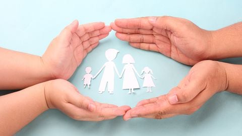 hands holding paper family cutout on blue background.