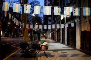 Una persona sin hogar duerme en una cama improvisada montada con un carro de la compra y un banco de la calle, en una zona decorada con banderas de Argentina, en Buenos Aires, Argentina, el miércoles temprano 27 de septiembre de 2023. (AP Foto/Natacha Pisarenko)