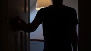 Silhouette of a man opening a door to a interior dark room, possibly a bedroom. He is an unrecognisable figure outlined be the landing light behind him.