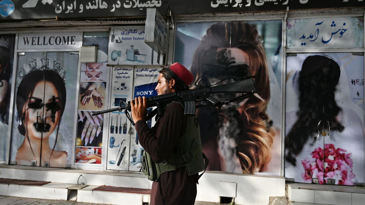 A Taliban fighter walks past a beauty salon with images of women defaced using spray paint in Shar-e-Naw in Kabul on August 18, 2021. (Photo by Wakil KOHSAR / AFP)