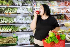 Mujer obesa comiendo una manzana mientras lleva un carrito de compras con verduras orgánicas en el mercado de abarrotes