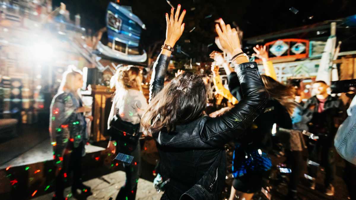 A young woman throwing her hands in the air, feeling the music and dancing energetically at a trendy open air nightclub