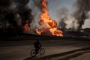 Archivo - Un hombre en su bicicleta pasa cerca de flamas y humo tras un incendio ocasionado por un ataque ruso en Járkiv, Ucrania, el 25 de marzo de 2022.
