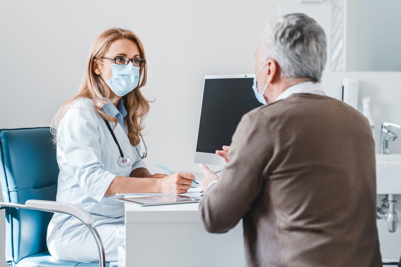 Mujer médico use mascarilla de protección hablando con el paciente en la oficina de la clínica.