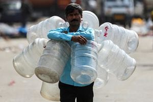 Un hombre camina con botellas de agua vacías alrededor del cuello para llenar agua que se venderá para beber en Nueva Delhi, India, 18 de mayo de 2023. 
