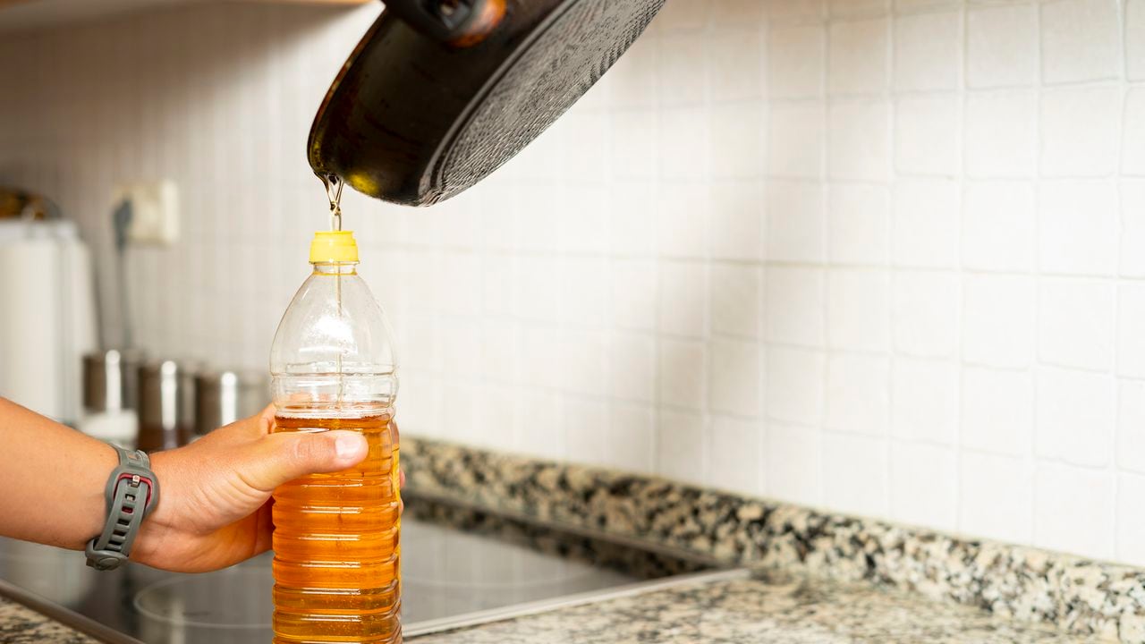 Close up of a man's hands recycling edible oil from a frying pan into a plastic bottle in his home kitchen.