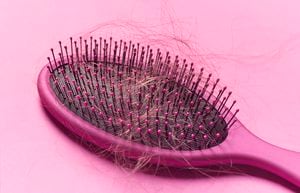 Close up of a brush with loose hair in it on a pink background