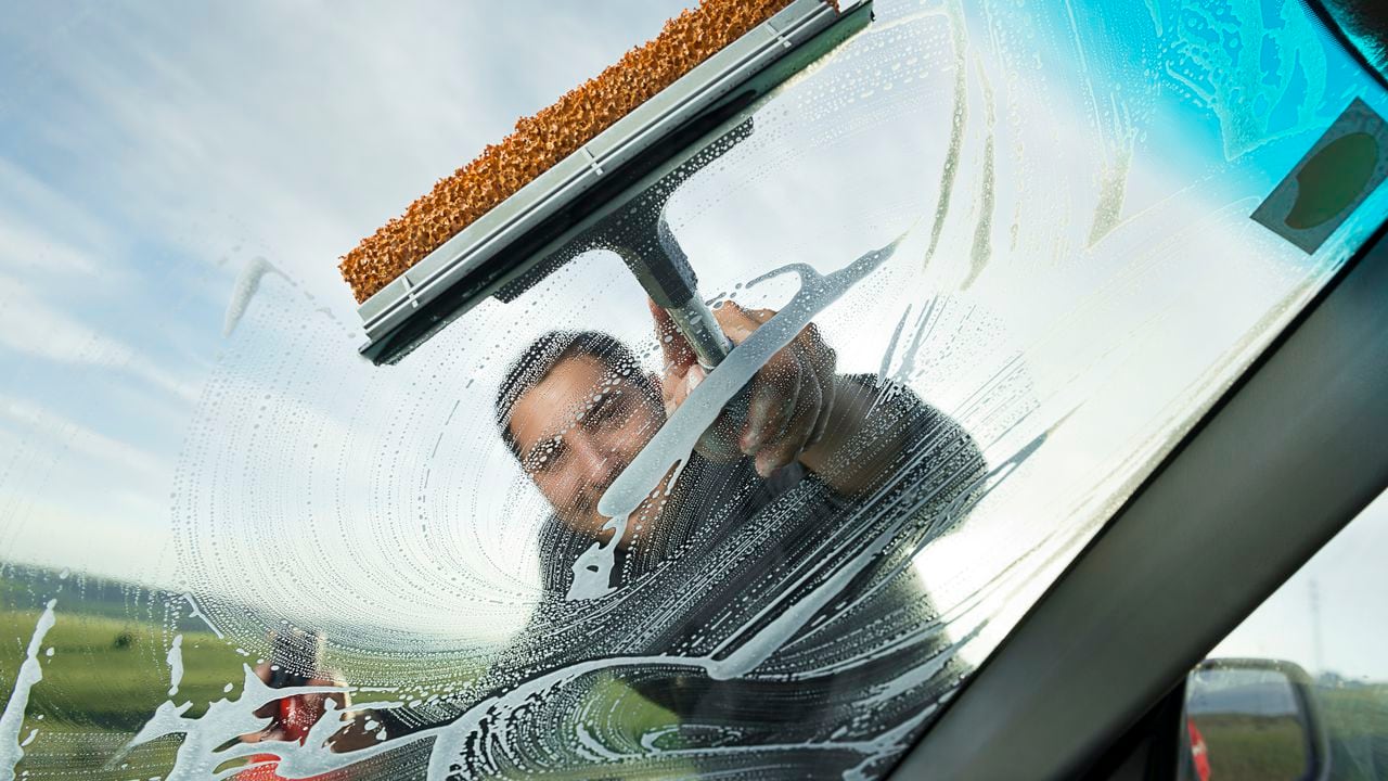 Adult man wiping windshield of his car.