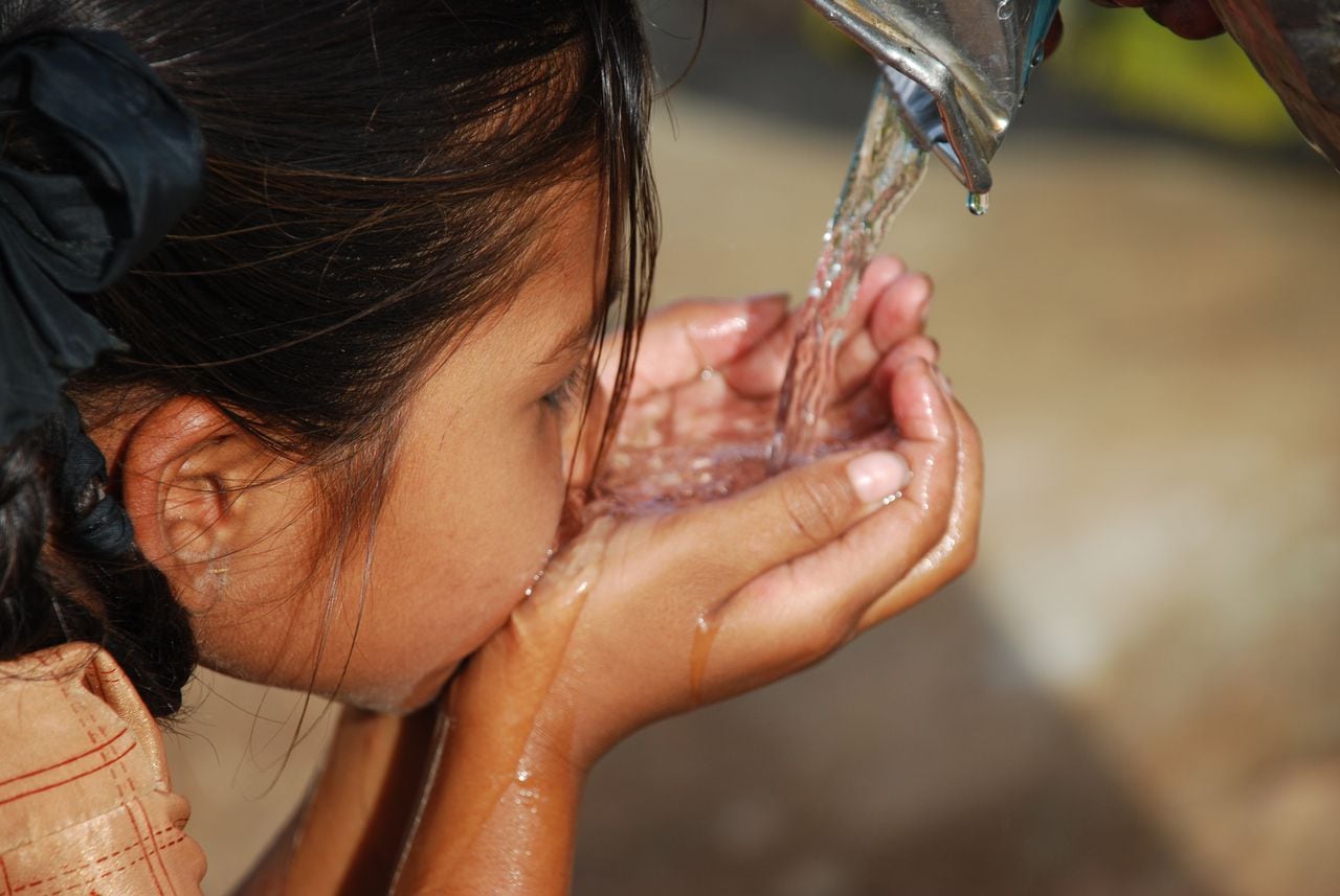 Pequeña niño de pelo oscuro bebiendo agua con sus manos, niña tomando agua.