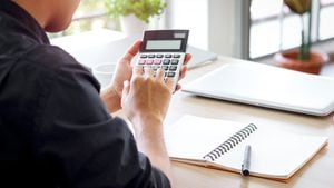 Empresario o contador Joven asiático sosteniendo una calculadora para calcular datos financieros, costos y presupuesto en el escritorio en casa, estadísticas contables y análisis de crédito para el pago.