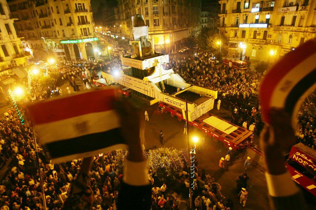 En esta foto de archivo tomada el 25 de agosto de 2006, los egipcios agitan su bandera nacional desde un balcón mientras se despiden de la estatua colosal de Ramsés II en la plaza de Talat Harb, al ser trasladada de la contaminada capital, El Cairo, a un lugar cercano a las pirámides de Giza, más cerca de su emplazamiento original. - Las momias de 18 reyes y cuatro reinas del antiguo Egipto desfilarán por las calles de El Cairo el 3 de abril por la noche, en una procesión de carnaval bautizada como el Desfile Dorado de los Faraones, al ser trasladadas desde una larga residencia en el Museo Egipcio para ser expuestas en el Museo Nacional de la Civilización Egipcia del sur de El Cairo.  Foto de Khaled DESOUKI / AFP.