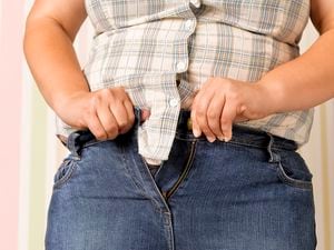 Adolescente obesa apretando un par de jeans demasiado apretados.