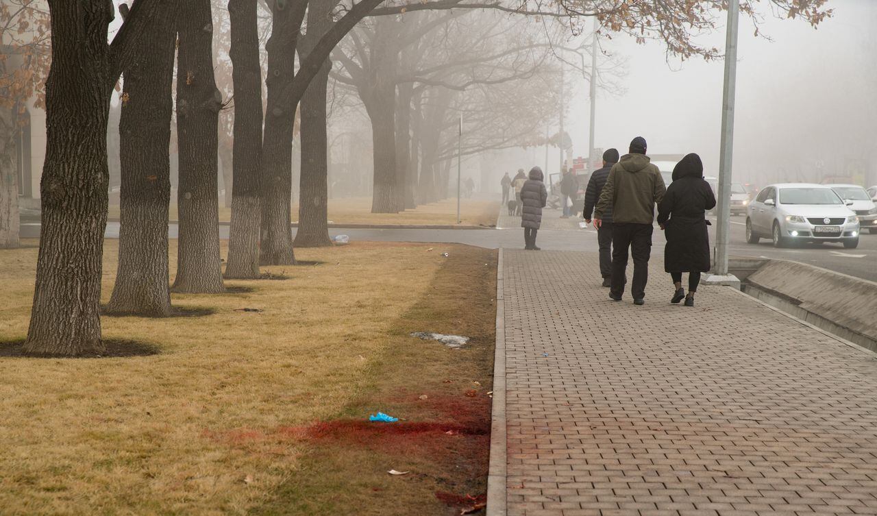 La gente camina junto a la sangre en un césped junto a la acera en el centro de Almaty el 6 de enero de 2022, luego de la violencia que estalló a raíz de las protestas por los aumentos en los precios del combustible.
