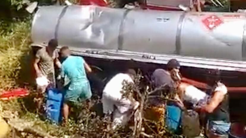 Un grupo de personas saquean el combustible del camión volcado con recipientes y tanques.