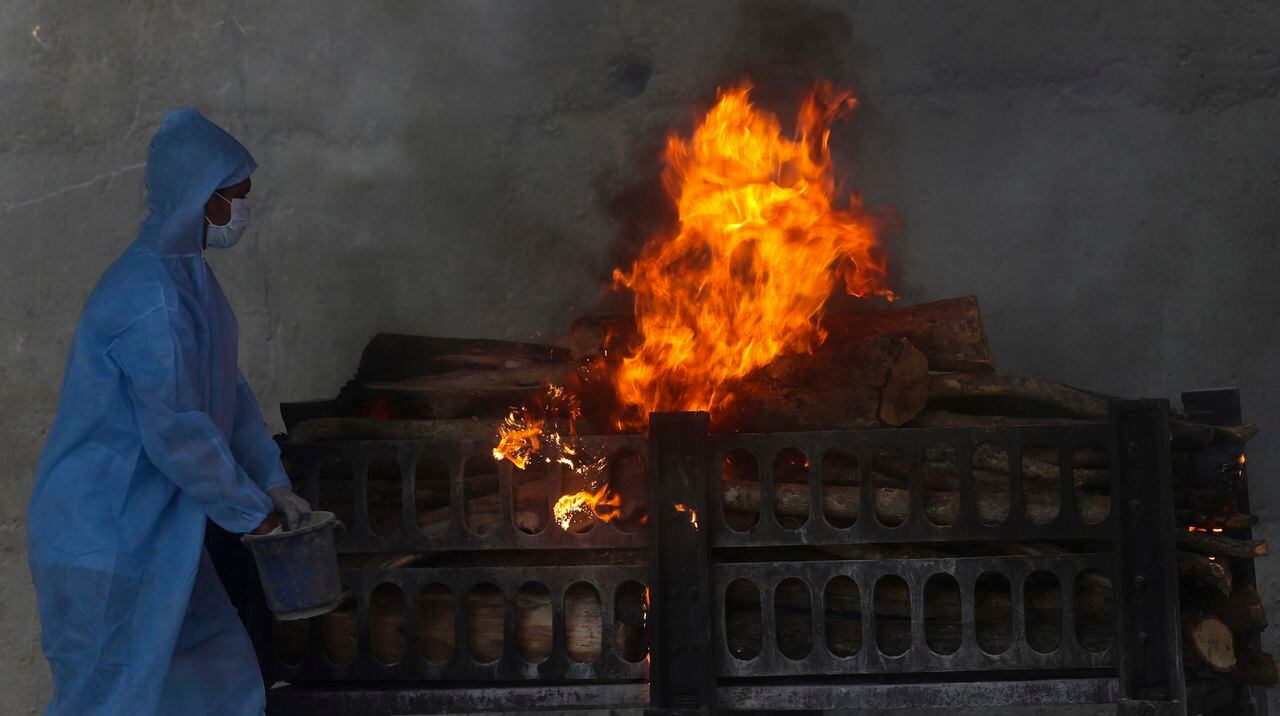 Un trabajador municipal con traje de protección personal realiza los últimos ritos durante la cremación de una víctima de COVID-19 en Vasai, en las afueras de Mumbai, India. (Foto AP / Rafiq Maqbool)