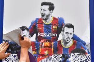 A worker removes posters featuring Barcelona's departing Argentinian forward Lionel Messi at the Camp Nou stadium in Barcelona on August 10, 2021. - France is waiting impatiently for Lionel Messi with supporters gathering outside Paris Saint-Germain's ground hoping to see the Argentine who is expected to join the Qatar-owned club after his exit from Barcelona. (Photo by Pau BARRENA / AFP)