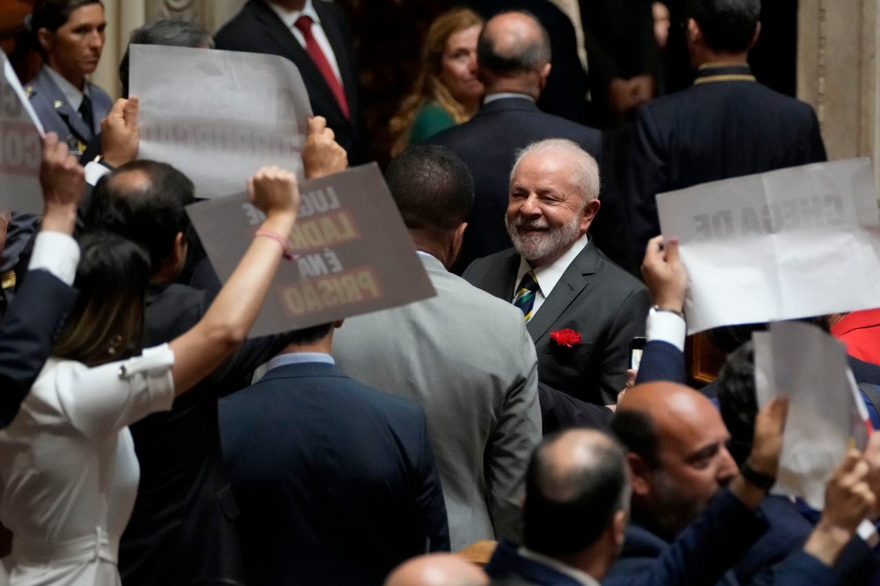 El presidente de Brasil, Luis Inácio Lula da Silva, sonríe mientras pasa junto a parlamentarios de extrema derecha que protestan por su presencia, luego de pronunciar un discurso durante una sesión de bienvenida en el parlamento portugués