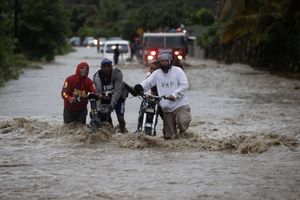 Personas cruzan con dificultad la carretera que se encuentra inundada producto de las intensas lluvias, hoy en San José de Ocoa (República Dominicana). EFE/Orlando Barría
