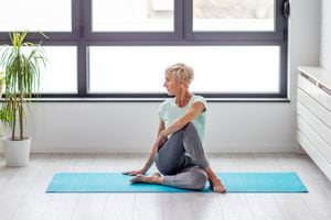 Mujer madura en ejercicio de pose de yoga en el apartamento en una alfombra con ventana al fondo