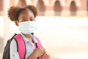 Back to school. African descent girl on school campus. She wears a mask for COVID-19, Coronavirus protection.