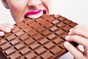Mujer en lápiz labial rosa mordiendo una gran barra de chocolate