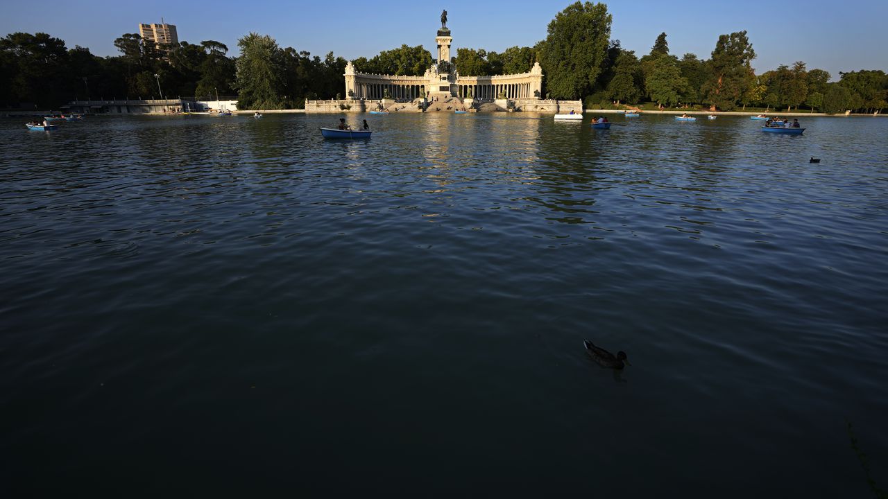 Algunas personas reman en el lago frente al monumento al rey Alfonso XII el viernes 23 de julio de 2021, en el Parque del Retiro, en Madrid, España. (AP Foto/Paul White)