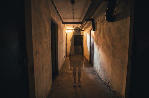 Scary girl in night gown in a dark basement hallway.