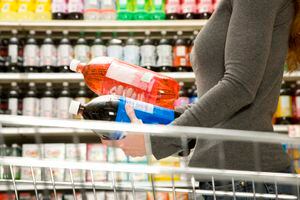 Mujer comparando ingredientes en botella de refresco, botella de gaseosa