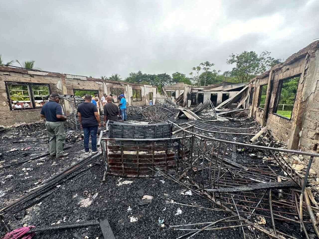 La gente se encuentra dentro de los restos de un dormitorio de una escuela secundaria quemado después de que varios niños, la mayoría de ellos de comunidades indígenas, murieran después de que un incendio destruyó el edificio durante la noche, en Mahdia, Guyana