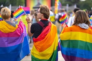 Wrapped in bisexual flag and pride flags this trio are waving small pride flags and watching a gay pride event