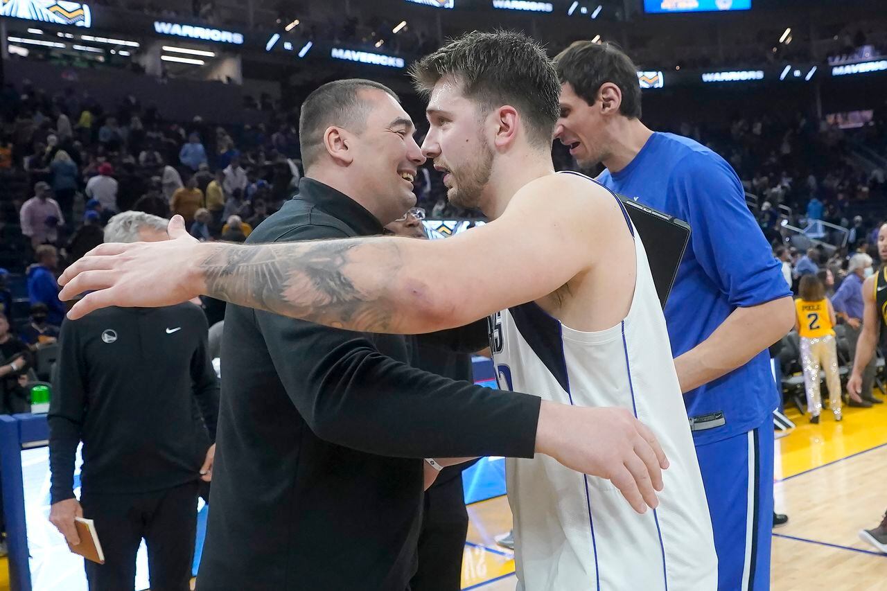 El entrenador asistente de los Golden State Warriors, Dejan Milojevic, en primer plano a la izquierda, abraza al guardia de los Dallas Mavericks, Luka Doncic, después de un partido de baloncesto de la NBA en San Francisco, el domingo 27 de febrero de 2022.